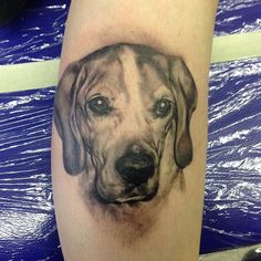 a black and white tattoo of a dog's face on the leg, it looks like he is looking straight ahead