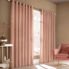 a pink chair sitting in front of a window with curtains on the windowsills