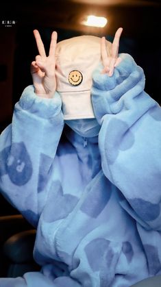 a person wearing a blue blanket covering their face and making the peace sign with both hands