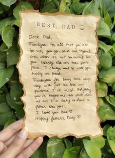 a hand holding up a piece of paper with writing on it and green leaves in the background