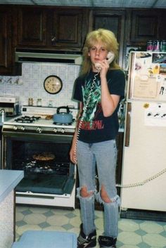 a woman talking on a cell phone while standing in a kitchen next to an oven