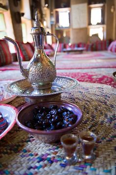 a table topped with plates and bowls filled with food next to a tea pot on top of a woven table cloth