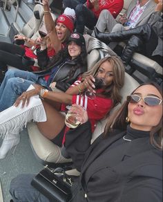 several women sitting in the bleachers at a baseball game drinking wine and laughing