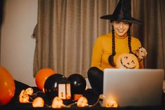 a woman dressed as a witch sitting in front of a laptop with halloween decorations around her