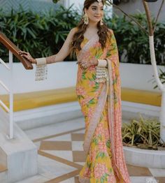 a woman in a yellow and pink sari is standing on the stairs with her arms outstretched