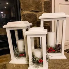 two white lanterns sitting on top of a counter next to each other with pine cones and red berries