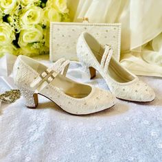 two pairs of white wedding shoes sitting on top of a table next to a bouquet