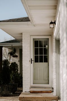 the front door of a white brick house with a light on it's side