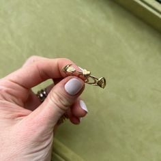 a woman's hand holding a gold ring on top of a green box with drawers in the background