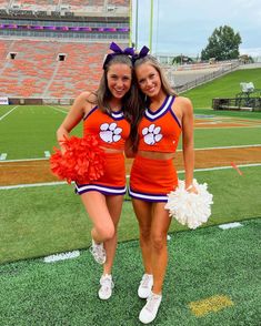 two cheerleaders pose for a photo on the field at an orange and white football game