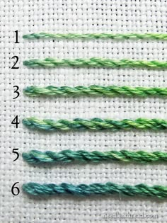 four different colors of thread on a white piece of cloth with numbers in the middle