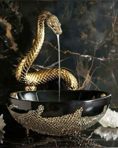 a gold and black bowl with a snake in it's mouth on a table