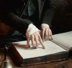 a person sitting at a table with an open book in front of them and their hands on top of it