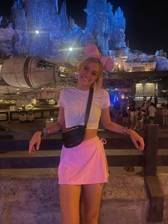 a woman posing for the camera in front of an amusement park at night with her hand on her hip