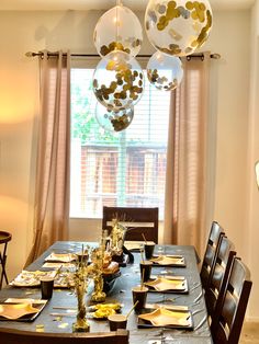 a dining room table set with place settings and balloons hanging from the ceiling above it