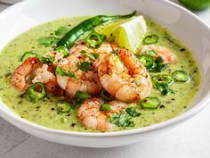 a white bowl filled with soup and garnished with shrimp, cilantro, and lime