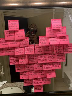 a person taking a selfie in front of a mirror with pink sticky notes on it