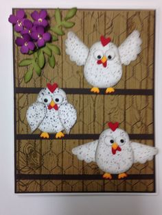 three white chickens sitting on top of a wooden fence with purple flowers in the background