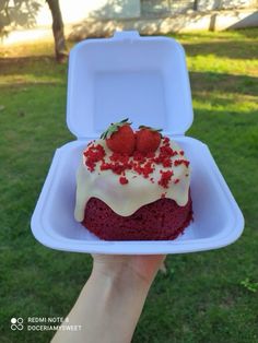 someone holding up a red velvet cake with white frosting and strawberries