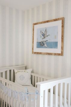 a baby's room with striped wallpaper and white crib bedding, framed art above the crib