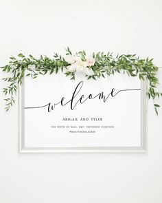 the welcome sign is surrounded by greenery and white flowers, which are on top of a silver frame