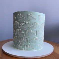 a blue cake with white frosting on a wooden table next to a gray wall