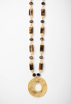 If you like to add layers of sparkle when dressing, then this gilt-edged necklace is for you. Draping Tiger is a long strand of tiger eye, gold and Swarovski© crystal with a large gold embossed pendant. This adjustable chain can be worn at different lengths. Get noticed in this glamorous, bold focal piece. Luxury Long Gold Beaded Necklace, Gold Beaded Amulet Necklace, Luxury Gold Long Necklace, Gold Beaded Medallion Jewelry, Gold Long Necklace With Large Pendant, Murano Glass Beads, Bridal Bracelet, Bridal Necklace, Bridal Earrings