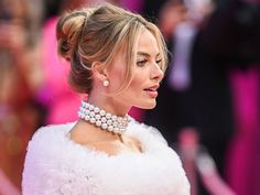 a woman in a white dress with pearls on her neck and hair pulled into a bun