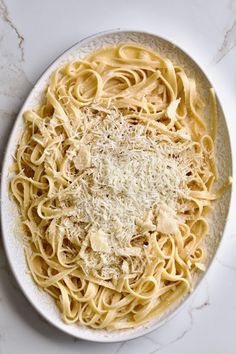 a white bowl filled with pasta covered in parmesan cheese on top of a marble counter