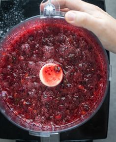 a person is pressing buttons on a blender with red liquid in the bottom half