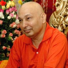 a bald man in an orange shirt sitting next to flowers