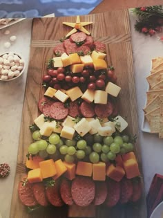 a christmas tree made out of cheese, meats and grapes on a cutting board