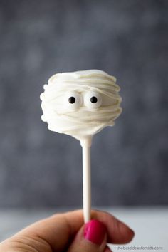 a close up of a person holding a cake on a stick with googly eyes