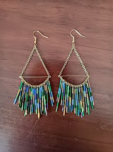 a pair of earrings with multi colored beads hanging from it's sides on a wooden surface