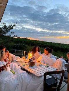 a group of people sitting around a table on top of a wooden deck next to the ocean