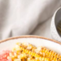 corn on the cob and red rice in a white bowl next to a fork