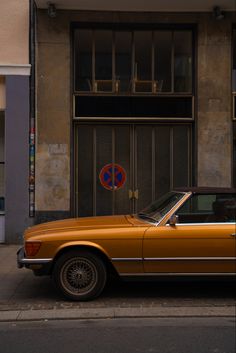 an orange car parked in front of a building on the side of the street with a no parking sign above it