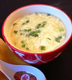 a red and white bowl filled with soup next to a spoon on top of a table