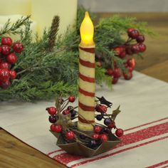 a lit candle sitting on top of a table next to some berries and greenery