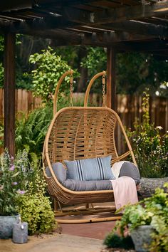 a wicker swing chair with blue cushions in a garden area next to a wooden pergolan