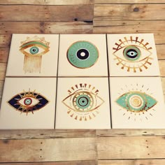 four square paintings with eye designs on them sitting on a wooden floor in front of a wall