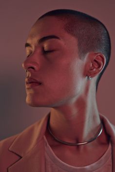 a woman with her eyes closed wearing a choker necklace and pink shirt, looking to the side