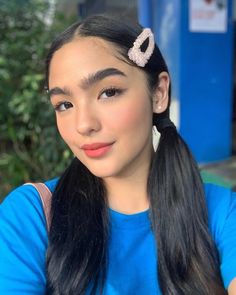 a woman with long black hair wearing a blue shirt and a pair of earrings on her head