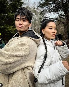 a man and woman standing next to each other in front of some trees with their arms wrapped around them