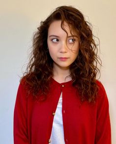 a young woman with curly hair wearing a red cardigan and white t - shirt