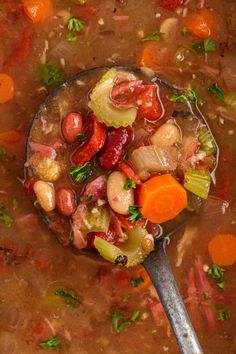 a ladle full of soup with carrots, beans and other vegetables in it