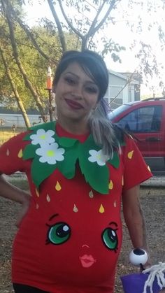 a woman in a red shirt is holding a purple bucket and wearing a strawberry costume