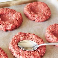 four hamburger patties on a baking sheet with a spoon