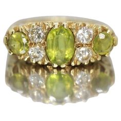 Vintage from the 1970s Materials: Stone Gemstone: Peridot Gem Color: Colorless Band Color: Gold 18K yellow gold, peridot & diamond ring Details: Diamonds 3mm diameter -- 4 x 0.10ct = 0.40ct Center Peridot 5 mm x 7mm approx Accent Peridots: 4mm round approx Weight: 6.4g Size: 6 Art Nouveau Carved Design possibly a Suffrage ring. Fully hallmarked makers stamp HBJ 750 Birmingham letter date B 1976 Large Moonstone Ring, Statement Rings Diamond, Buckle Ring, Cushion Ring, Cushion Cut Ring, Victorian Rings, Sapphire Diamond Ring, Peridot Ring, Modern Ring