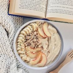 an open book is next to a bowl of cereal and apple slices on a table